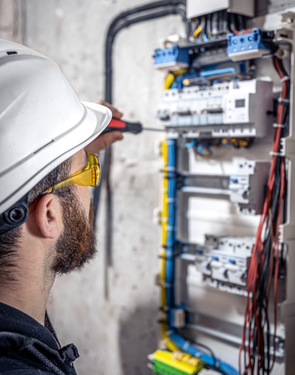 A male electrician works in a switchboard with an electrical connecting cable, connects the equipment with tools.
