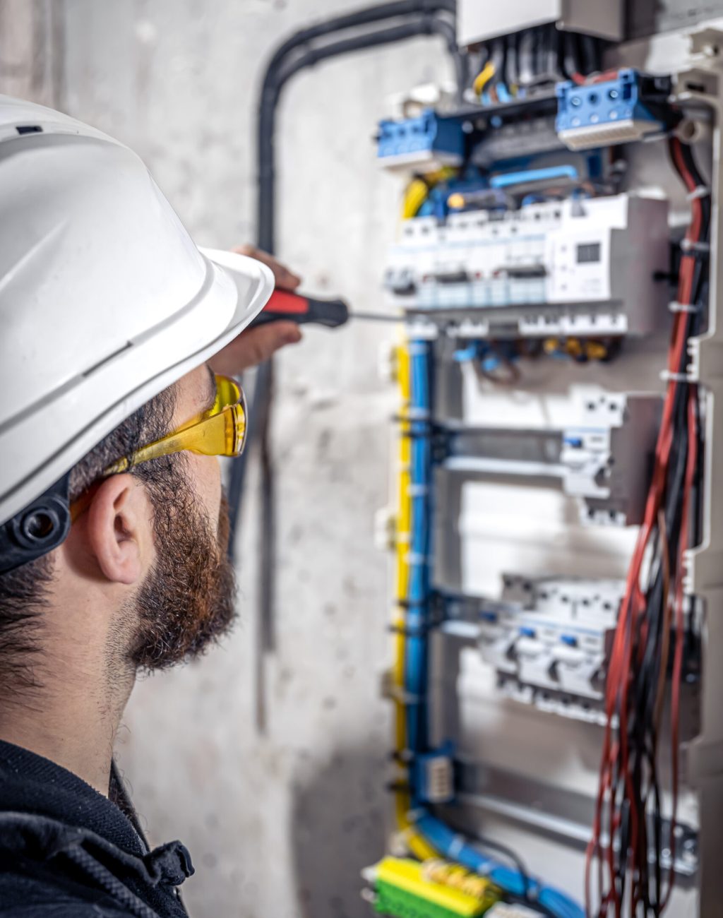 A male electrician works in a switchboard with an electrical connecting cable, connects the equipment with tools.